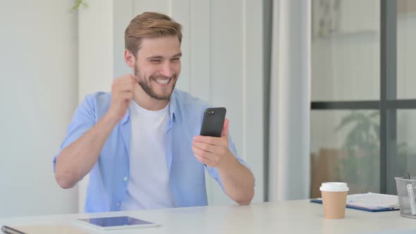 Young Creative Man Celebrating Success on Smartphone in Office