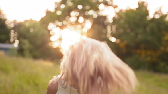 Young Blonde Teen Girl Walking in Summer Sunset Park Looks at Camera with