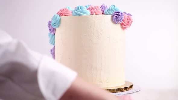 Baker piping pastel color buttercream rosettes on a white cake to make a unicorn cake.