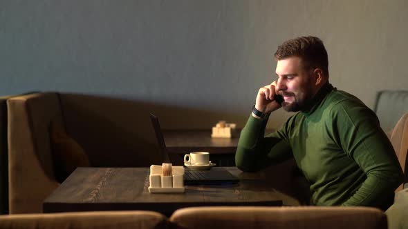 Businessman Talking Phone While Working with His Laptop in the Cafe