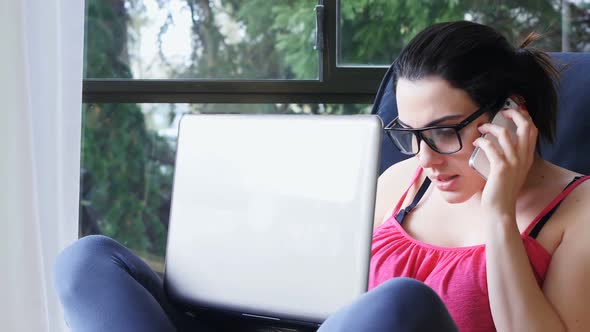 Beautiful woman using laptop while talking on mobile phone