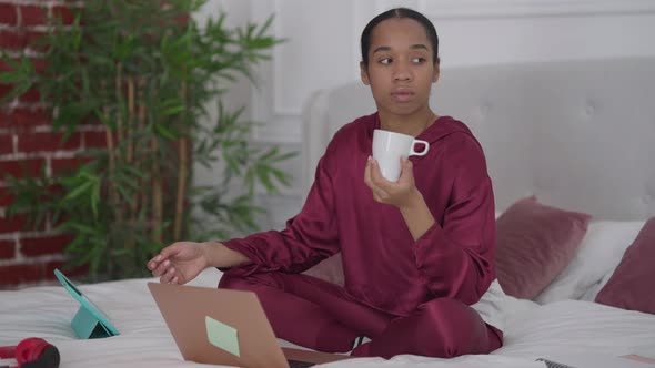 Portrait of Young Troubled Woman Sitting on Bed Holding Coffee Cup Thinking