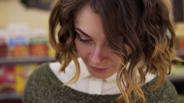 Young Curly Haired Woman Doing Grocery Shopping at the Supermarket She is Reading a Product Label