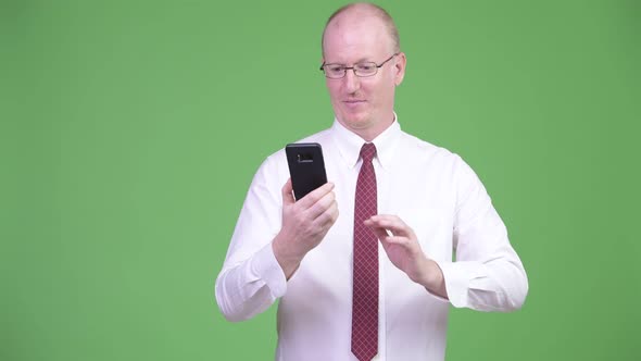 Happy Mature Bald Businessman Using Phone and Getting Good News