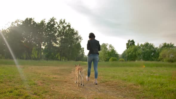 Attractive Woman in Headphones Walks with Her Dog in the Park.