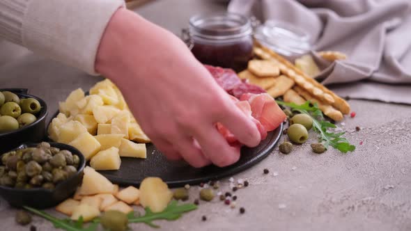 Making Meat and Cheese Antipasto Plater Woman Putting Pieces of Prosciutto Ham on Stone Serving