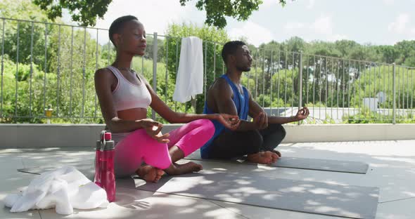 African american couple practicing yoga sitting meditating on sunny garden terrace