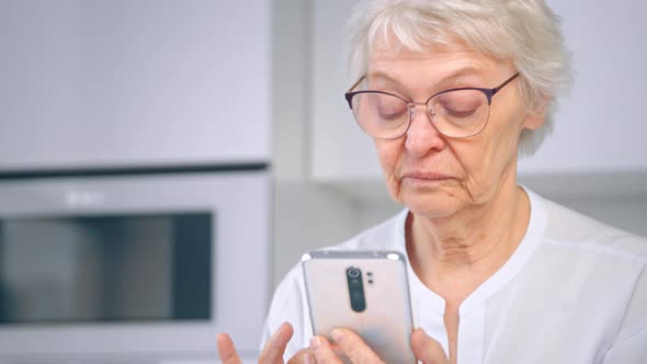 Aged woman manager in glasses and white blouse scrolls social media on smartphone