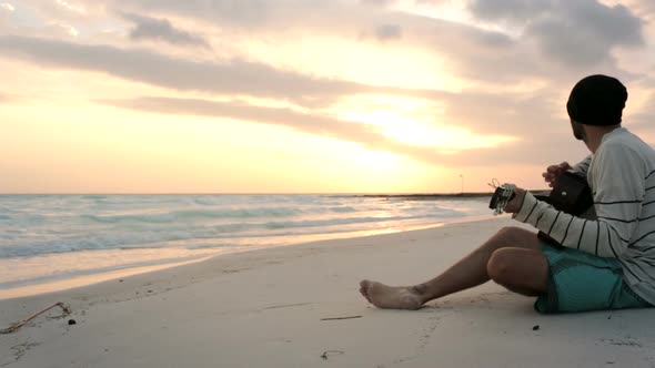 Young Beautiful Man Plays Guitar at Ocean Beach Seaside at Sunrise or Sunset in Summer Gimbal