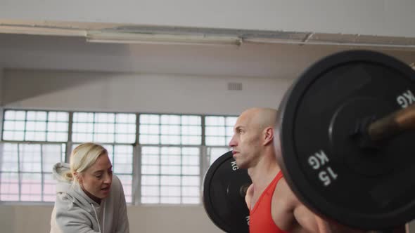 Caucasian muscular man lifting weight bar with female coach