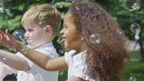 Cute Girl and Boys Enjoying Playing with Soap Bubbles alt