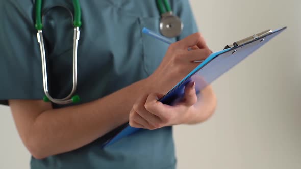 Closeup Cropped Shot of Unrecognizable Female Doctor in Green Medical Suit Writing Notes on