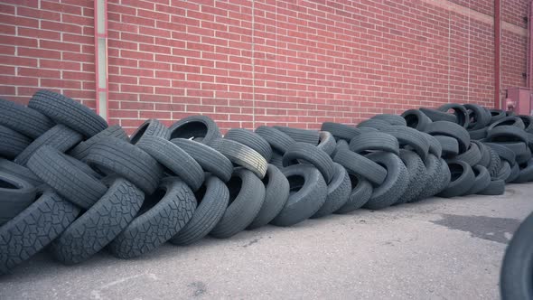 Caucasian male stacking old used tires in front of a brick wall to be recycled, static