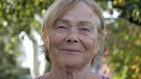 Portrait Of Elderly Woman 80s With Wrinkles Looking At Camera Grinning In Garden