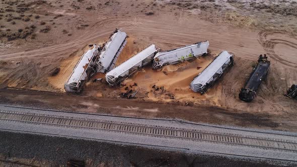 Train cars wrecked on the side of the tracks with load spilled out into the dirt