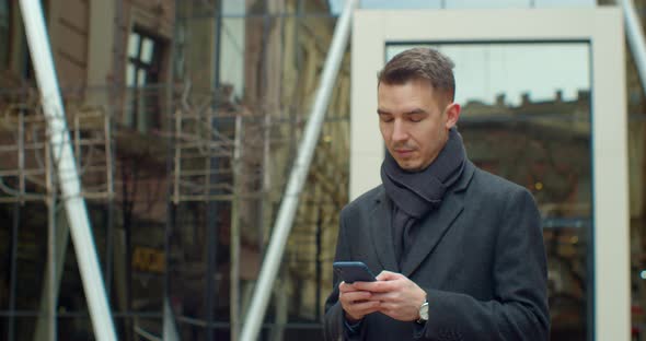 Portrait of Man Using Smartphone Near Modern Office Center. Chatting in Social Networks with His