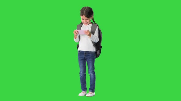 School Girl with Backpack Watching Something Funny on Her Pink Phone and Laughing on a Green Screen