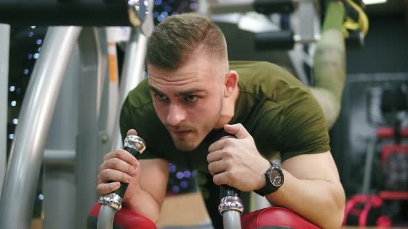 The Young Athletic Man Lifting Weights By His Legs on Fitness Equipment in Gym Looking Forward