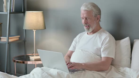 Successful Old Man with Laptop Celebrating in Bed