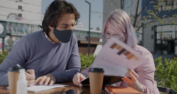 Arab Guy Working Outdoors with Caucasian Colleague Drinking Coffee Wearing Mask During Pandemic