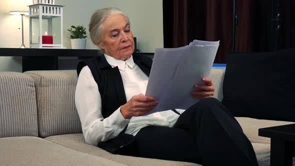 Old Caucasian Woman Reads Some Documents in Living Room