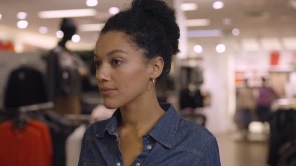 Beautiful African American Woman Choosing Clothes Hanging on Hangers in Trendy Clothing Store