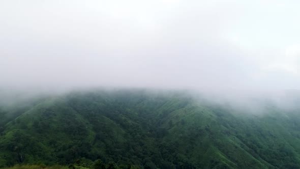 Dense fog covering top of mountain with lush forest after last rains of autumn season in India