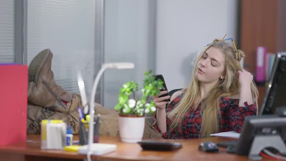 Relaxed Carefree Hipster with Feet on Table Surfing Internet on Smartphone Chewing Gum