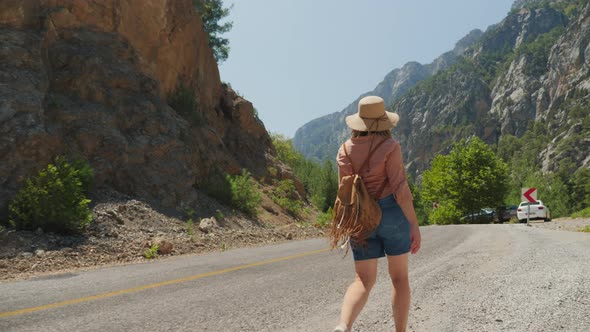Young Woman Hiking Walks Along the Road Between High Mountains