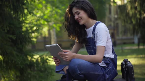 Beautiful Relaxed Caucasian Woman Laughing Watching Social Media on Tablet Sitting on Bench at