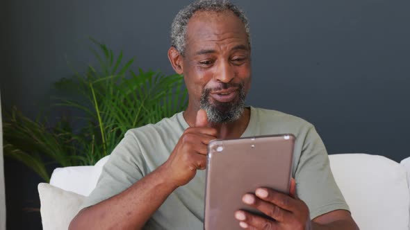 Senior african american man having a video call on digital tablet while sitting on the couch at home