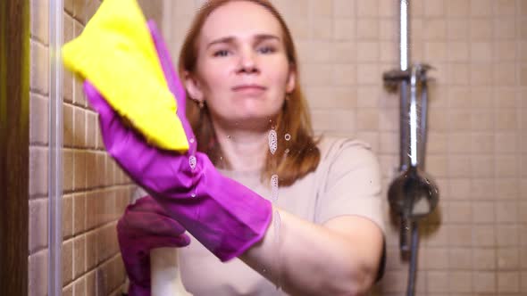 Woman in Gloves with Detergent Spray Rag Washes a Partition in the Shower