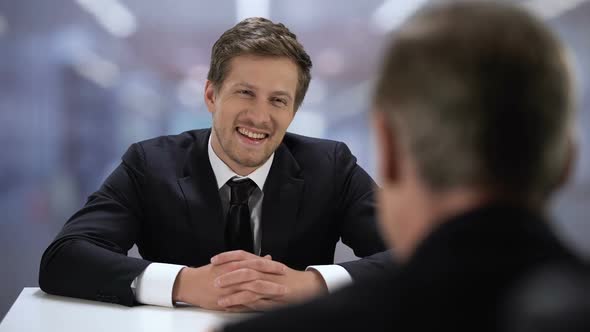 Young Businessman Talking With Adult Partner During Meeting, Laughing and Joking