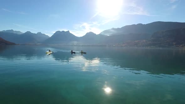 Three kayakers paddle in a scenic mountain lake.