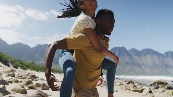 African american man giving piggyback ride to his wife at the beach