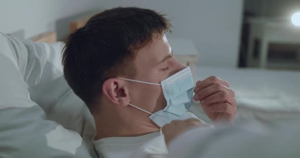 Portrait of Ill Dying From Virus Man in Medical Mask Lying and Coughing on Bed