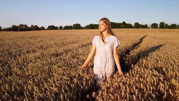 Beautiful young girl walking alone in the agricultural field of golden rye, slow mo