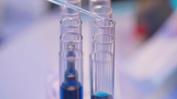 Close Up of Pipette Dropping Samples of Color Liquid Into Test Tubes in Laboratory