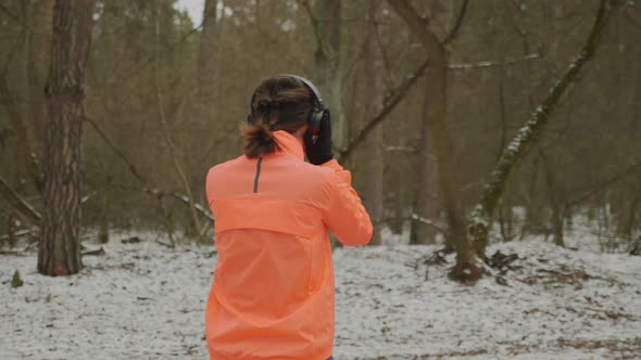 Woman starts her running training wearing black headphones in winter snow park. Marathon concept
