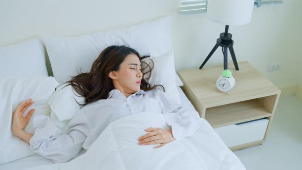 Asian girl in pajamas look at alarm clock and awake from sleep in hurry and fast due to oversleep.