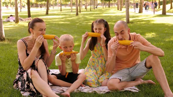 A Happy Family in the Park Eating Corn They are Sitting on the Green Grass