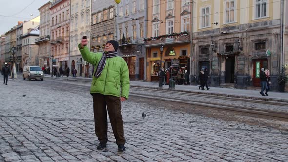 Senior Man Grandfather Tourist Is Making Online Video Call with Smart Phone in Winter City Center