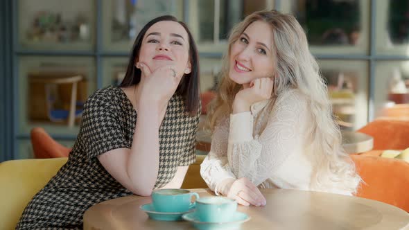 Two Positive Happy Women Posing at Table in Cafe