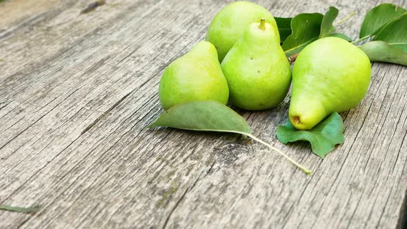 Fresh pears are tossed and rolled on a wooden surface.