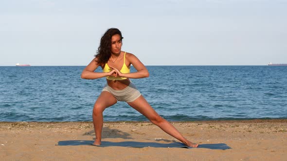 Beautiful tanned young woman sitting in a meditation pose on the beach. Goods for health.