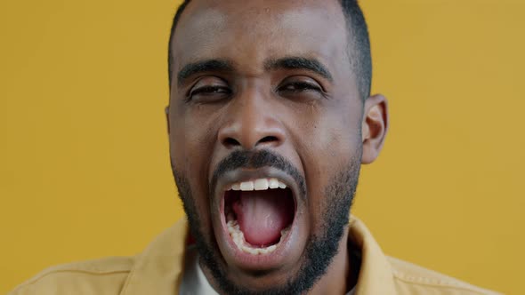 Closeup Portrait of Tired Young Man Yawning and Looking at Camera on Yellow Background