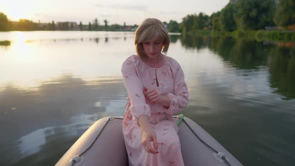 Concentrated Queer Person Touching Sleeves of Pink Dress Sitting in Boat on Summer Lake