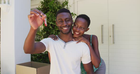 Portrait of smiling african american couple holding house keys and embracing outside their home