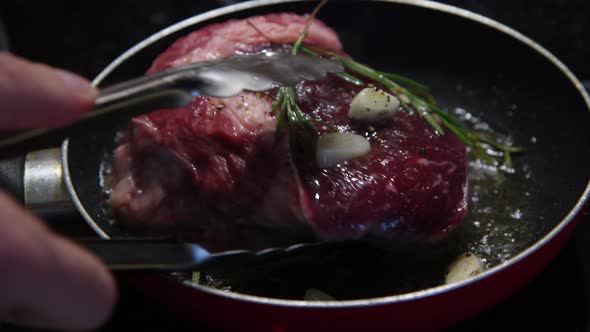 Person turns over frying steak