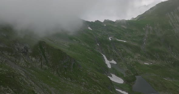 aerial footage of mountain lake and mountain range with snow and peaks in clouds